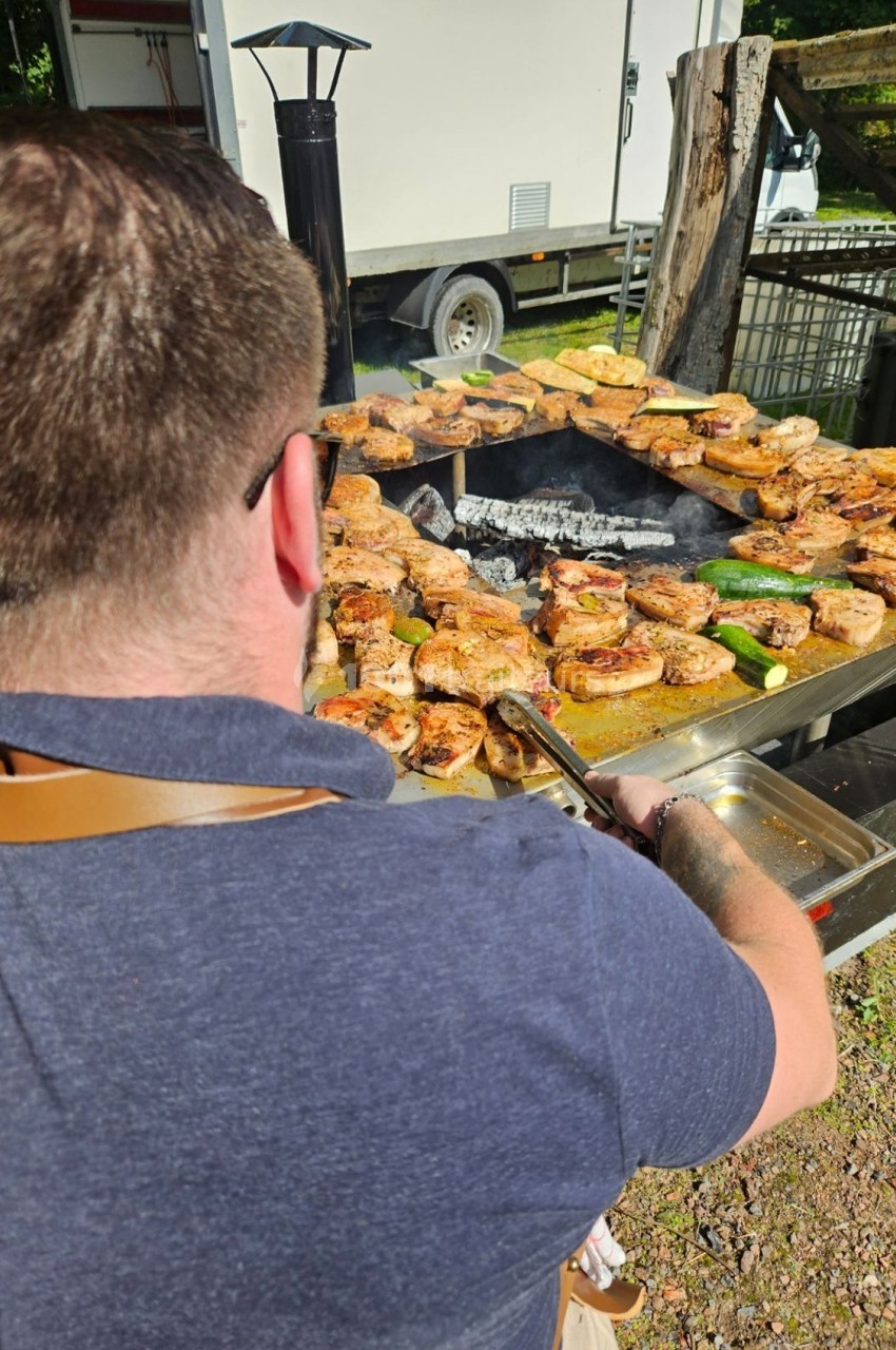 Un homme en train de griller des viandes et des légumes sur un barbecue en plein air.