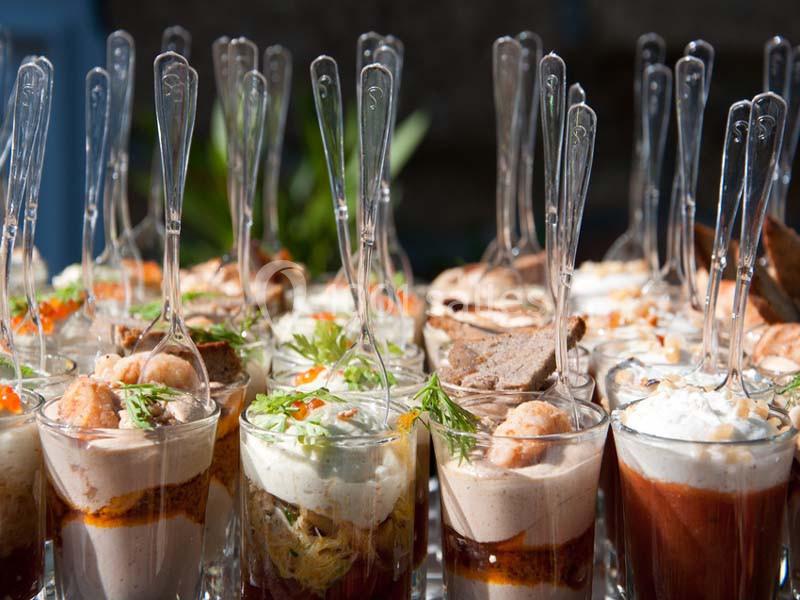 Verrines variées garnies de crevettes, mousse, légumes et crème, présentées avec des cuillères transparentes.