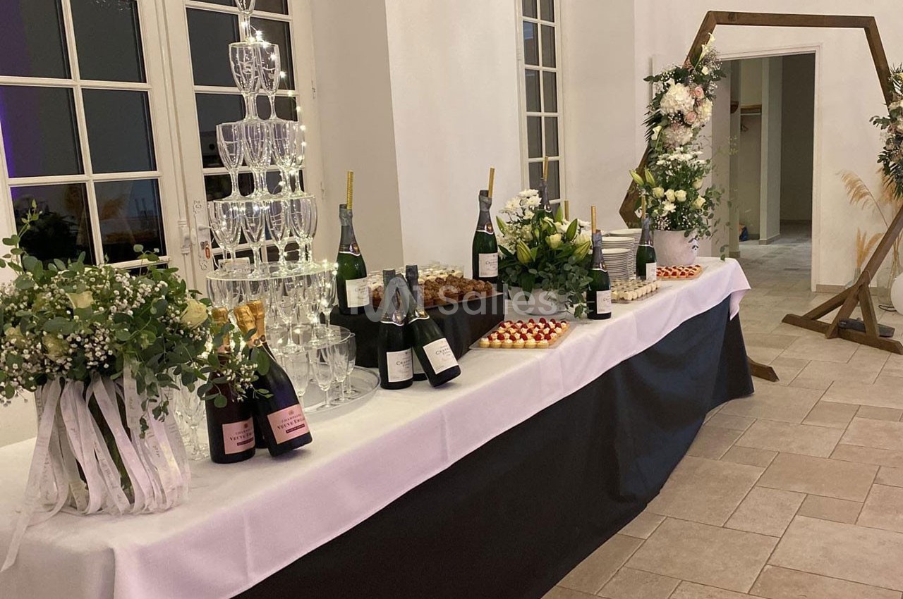 Table décorée avec des bouteilles de champagne, une pyramide de verres, des fleurs et des desserts dans une salle lumineuse.