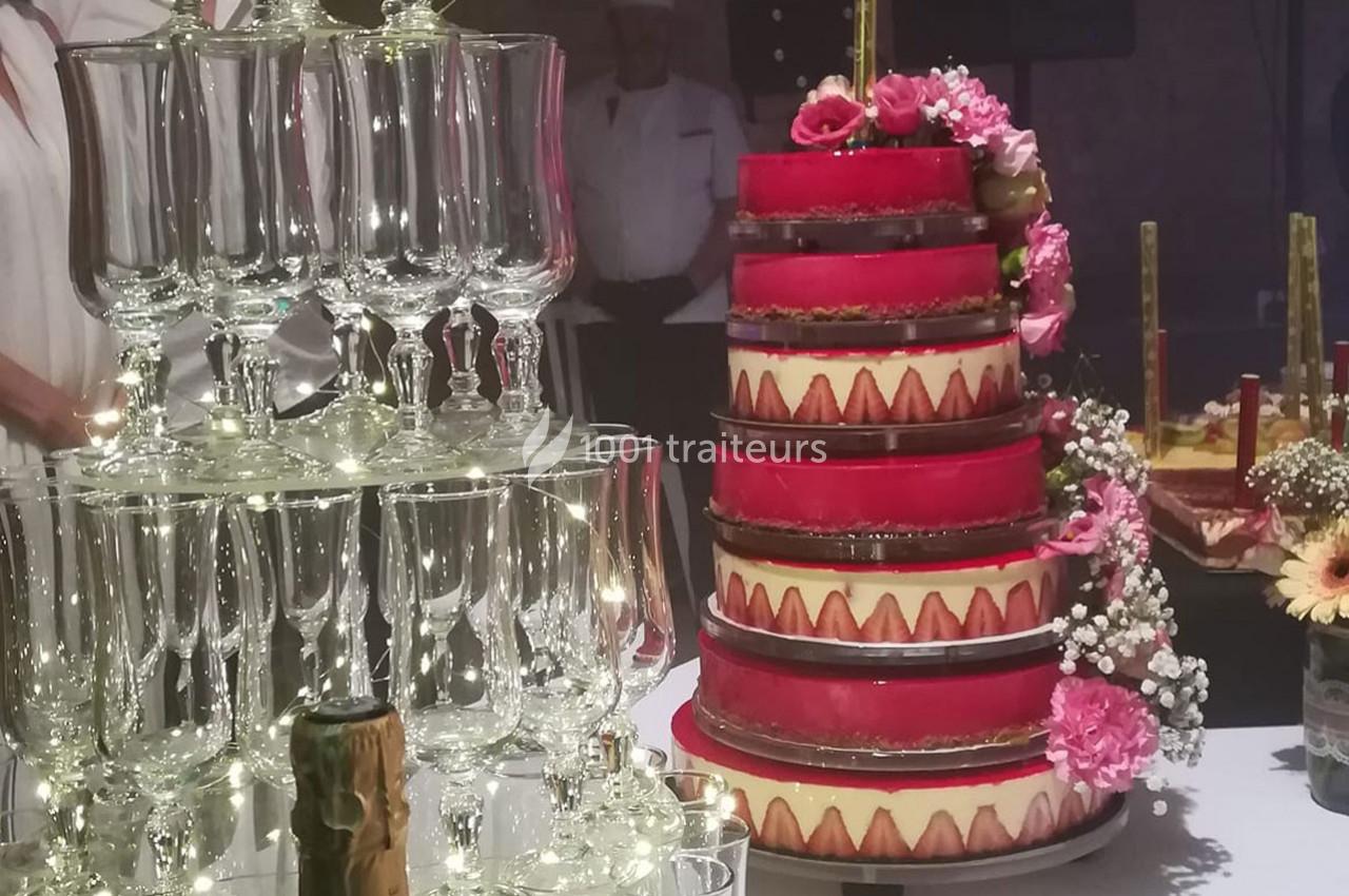Tour de coupes en verre illuminée et gâteau à étages décoré de fleurs roses sur une table de réception.