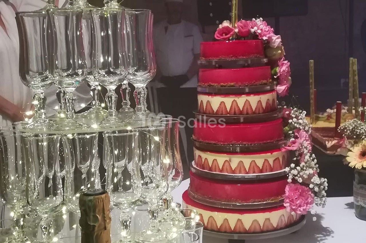Tour de coupes en verre illuminée et gâteau à étages décoré de fleurs roses sur une table de réception.