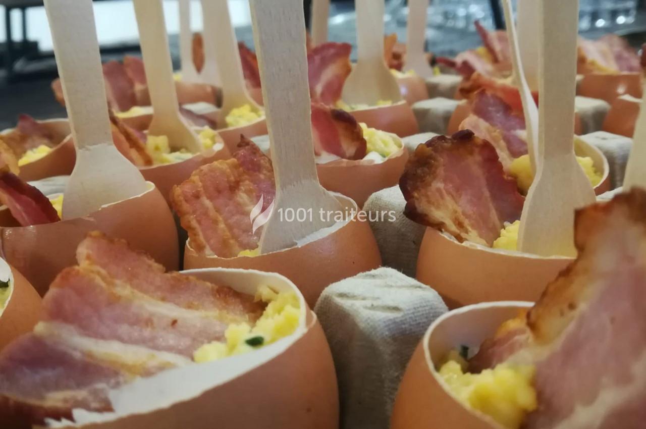 Œufs coquilles garnis d'œufs brouillés et de tranches de bacon, présentés avec des cuillères en bois.