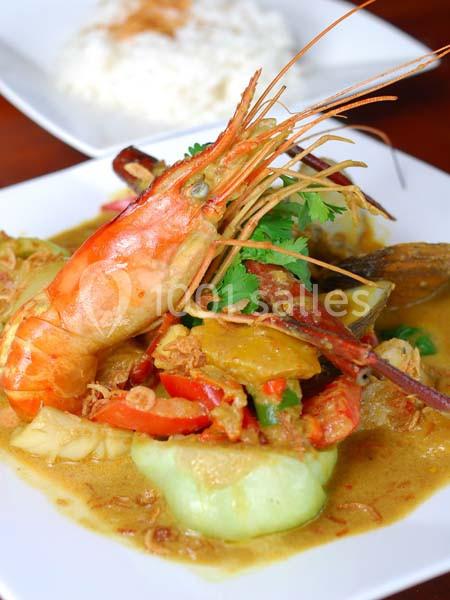 Crevette entière servie dans un curry jaune avec légumes, présentée dans une assiette blanche.