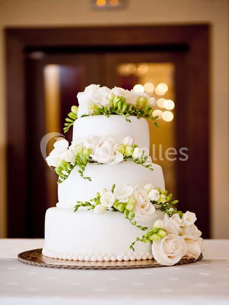 Gâteau de mariage à trois étages décoré de fleurs blanches et vertes, posé sur une table blanche.
