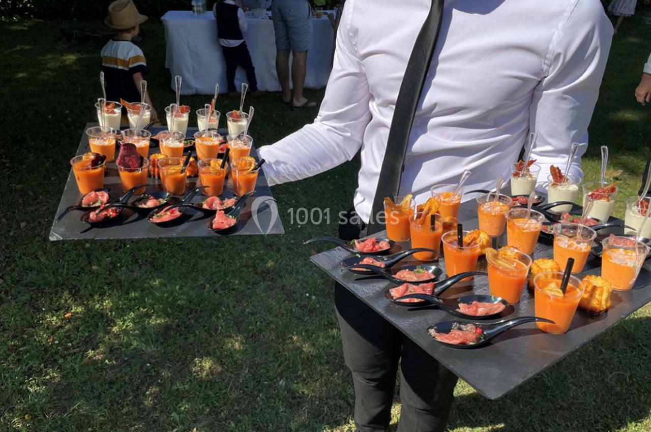 Serveur tenant deux plateaux de verrines et amuse-bouches variés lors d'un événement en extérieur.