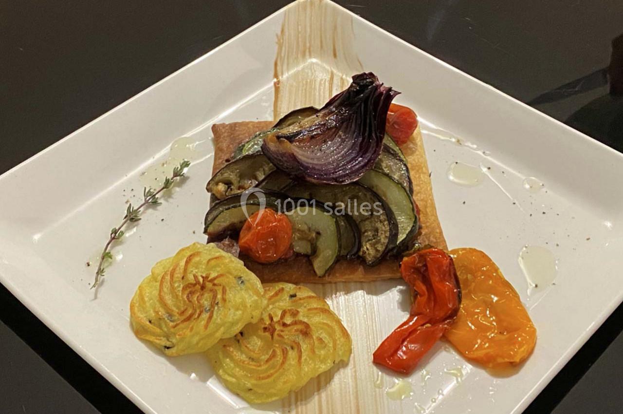 Tarte fine garnie de légumes grillés, accompagnée de pommes duchesse et de poivrons rôtis sur une assiette blanche.