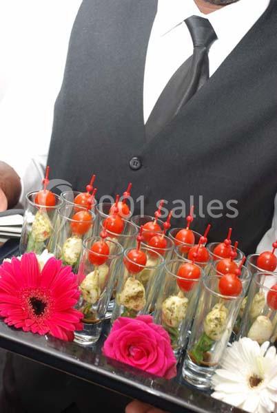 Un serveur présente un plateau de verrines garnies de tomates cerises et de fleurs décoratives.