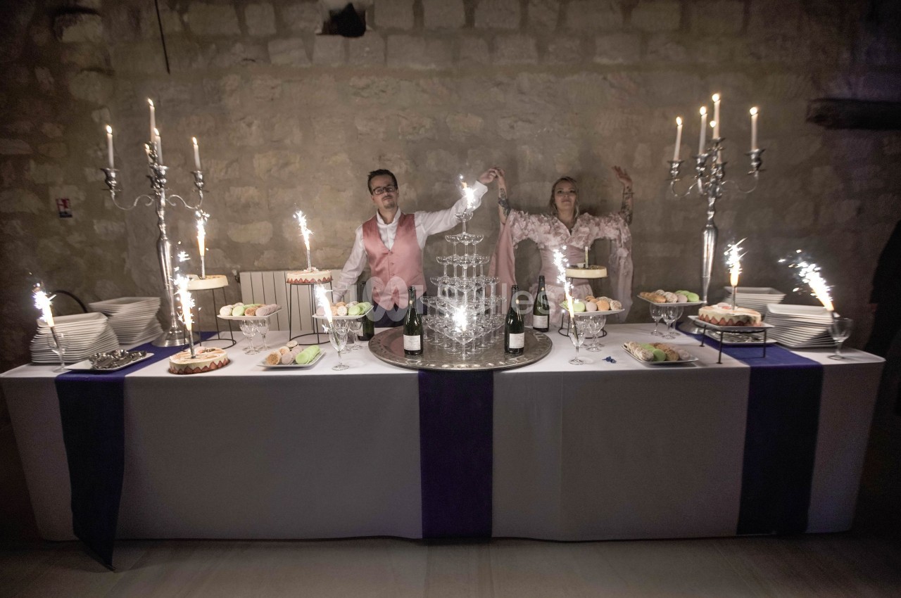 Un couple debout derrière une table de réception décorée, entourée de chandeliers et de desserts, avec une fontaine à…