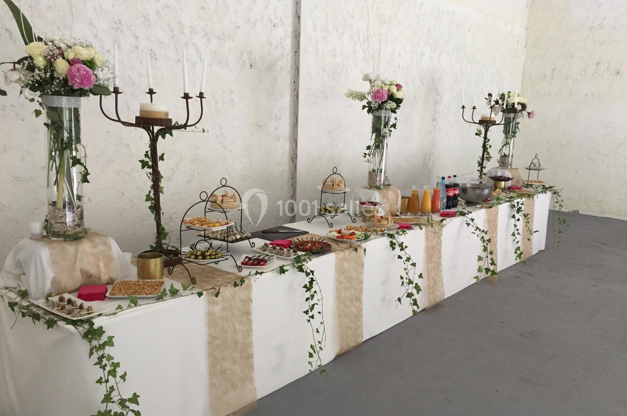 Table de buffet décorée avec des fleurs, des chandeliers et des plats variés, dans une salle aux murs clairs.