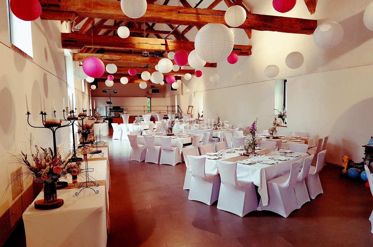 Salle de réception décorée avec des lanternes suspendues et des tables rondes dressées avec nappes blanches.