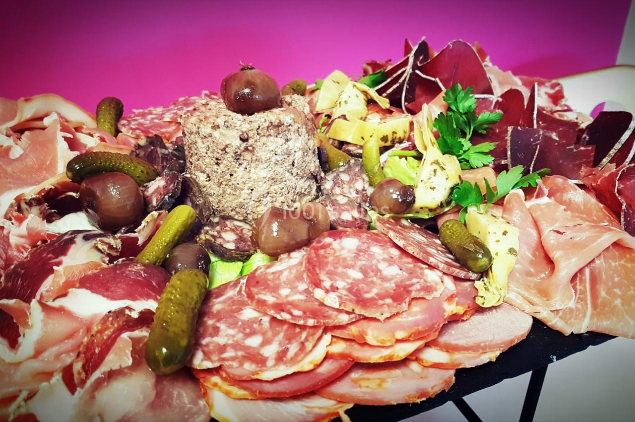 Plateau de charcuterie variée avec jambon, saucisson, cornichons, champignons et décorations sur fond rose.