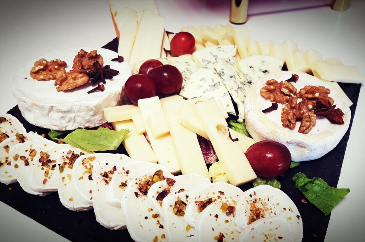 Plateau de fromages variés avec noix, raisins, feuilles de salade et tranches de fromage disposés sur une ardoise.