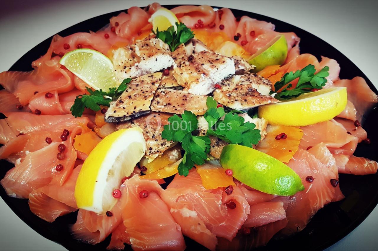 Assiette garnie de tranches de saumon fumé, morceaux de poisson grillé, rondelles de citron et herbes fraîches.