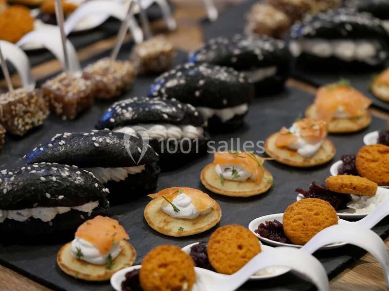 Assortiment de bouchées apéritives comprenant mini-burgers noirs, blinis au saumon et autres amuse-bouches variés.
