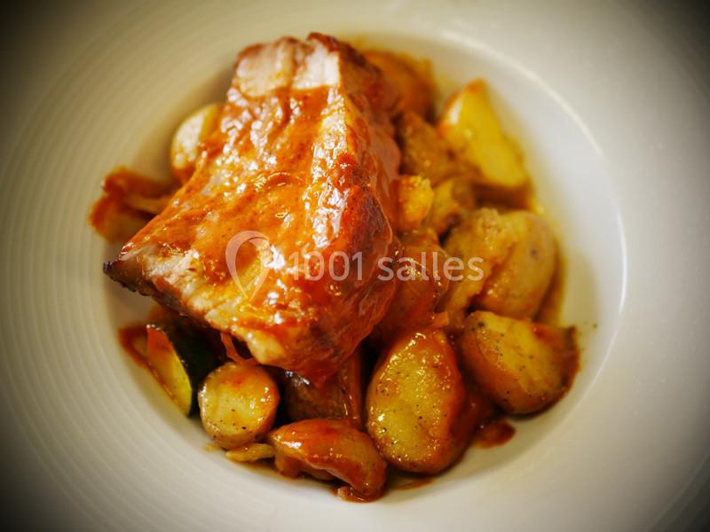 Plat de viande braisée accompagnée de pommes de terre et légumes, nappé d'une sauce dorée.