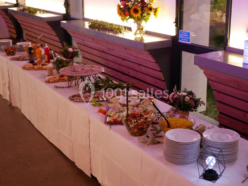 Buffet avec plats variés, salades, charcuteries, condiments et assiettes disposés sur une longue table blanche.
