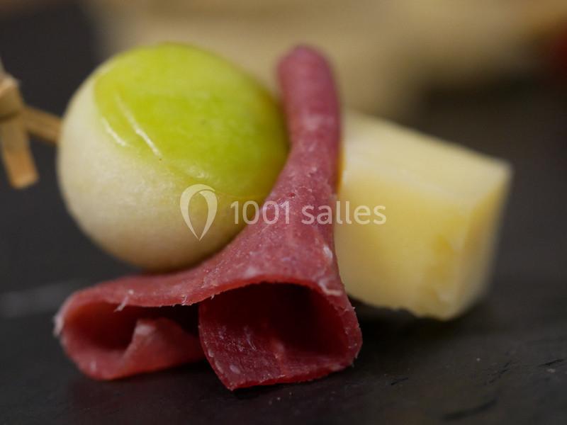 Tranche de viande séchée enroulée, cube de fromage et bille de melon sur une brochette en bois.