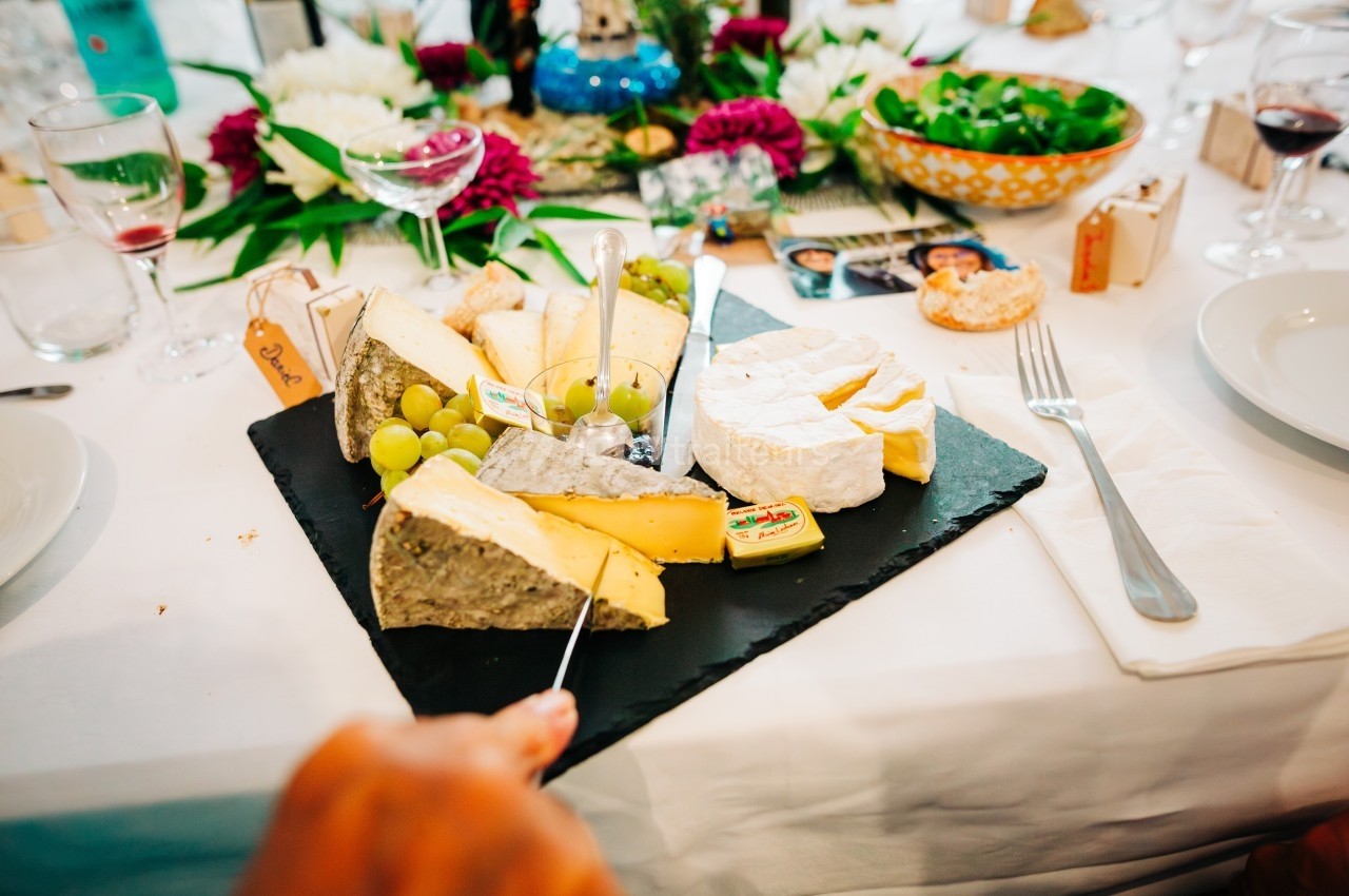 Plateau de fromages variés avec raisins et couteau, présenté sur une table dressée avec des fleurs et des plats.