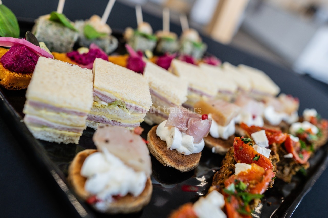 Plateau de canapés variés comprenant sandwichs, toasts garnis et bouchées apéritives colorées.