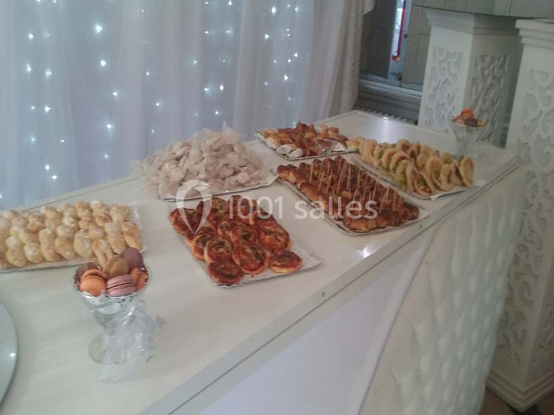 Buffet avec divers amuse-bouches, pâtisseries, toasts et macarons disposés sur une table blanche décorée.