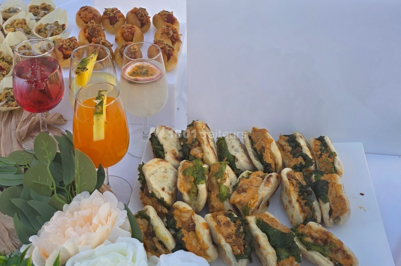 Plateau de mini-sandwichs garnis, accompagnés de cocktails colorés et de petites bouchées apéritives sur une table décorée.