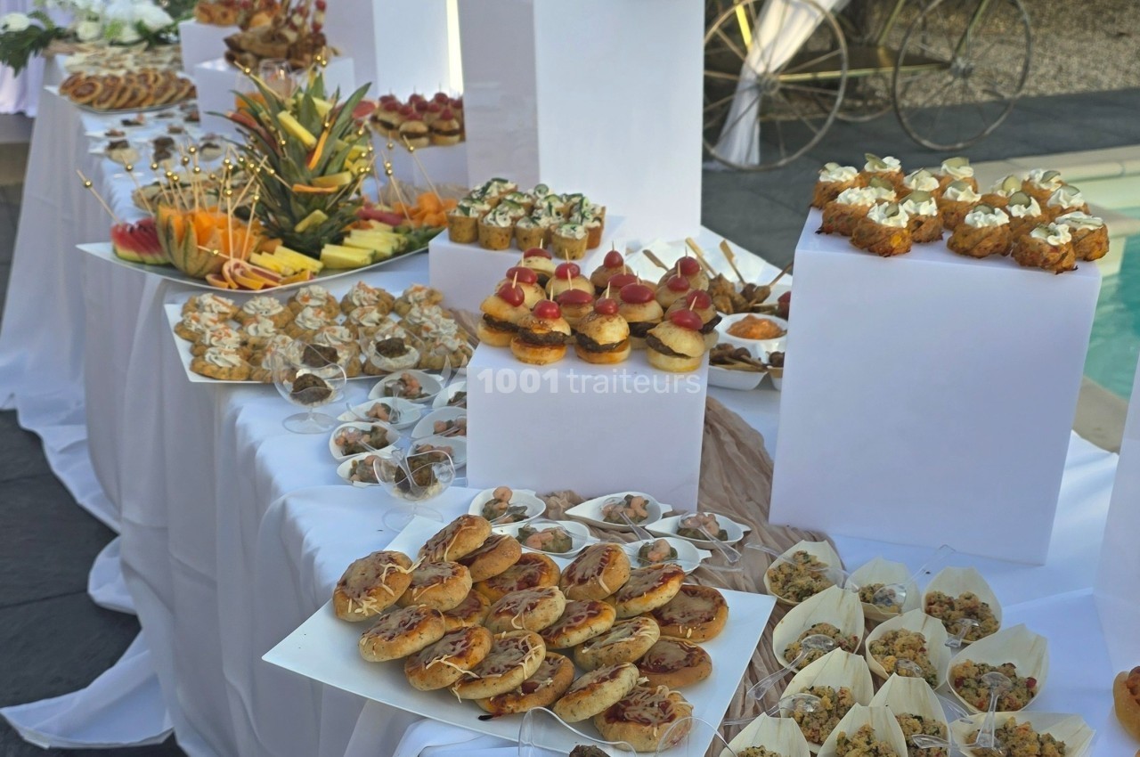 Buffet de réception avec une variété de bouchées salées et sucrées présentées sur des tables drapées de nappes blanches.