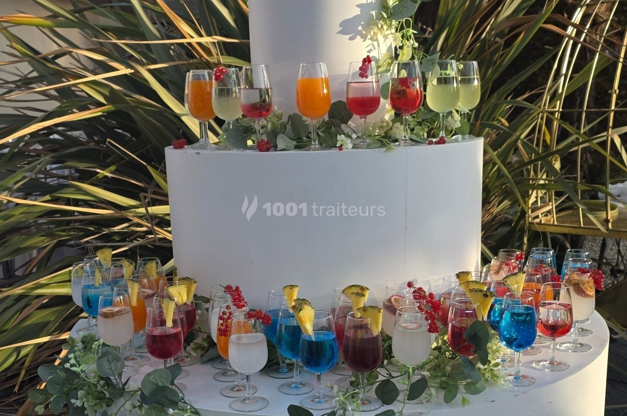 Présentoir circulaire décoré de feuillage, garni de verres colorés contenant des cocktails garnis de fruits.