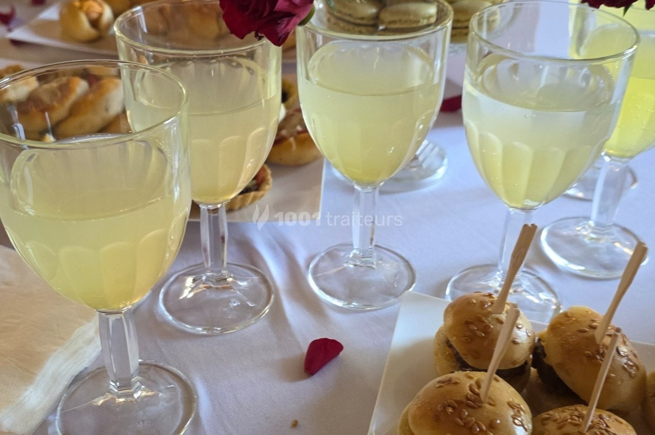 Verres de limonade sur une table blanche, entourés de petits pains, macarons et pétales de rose.