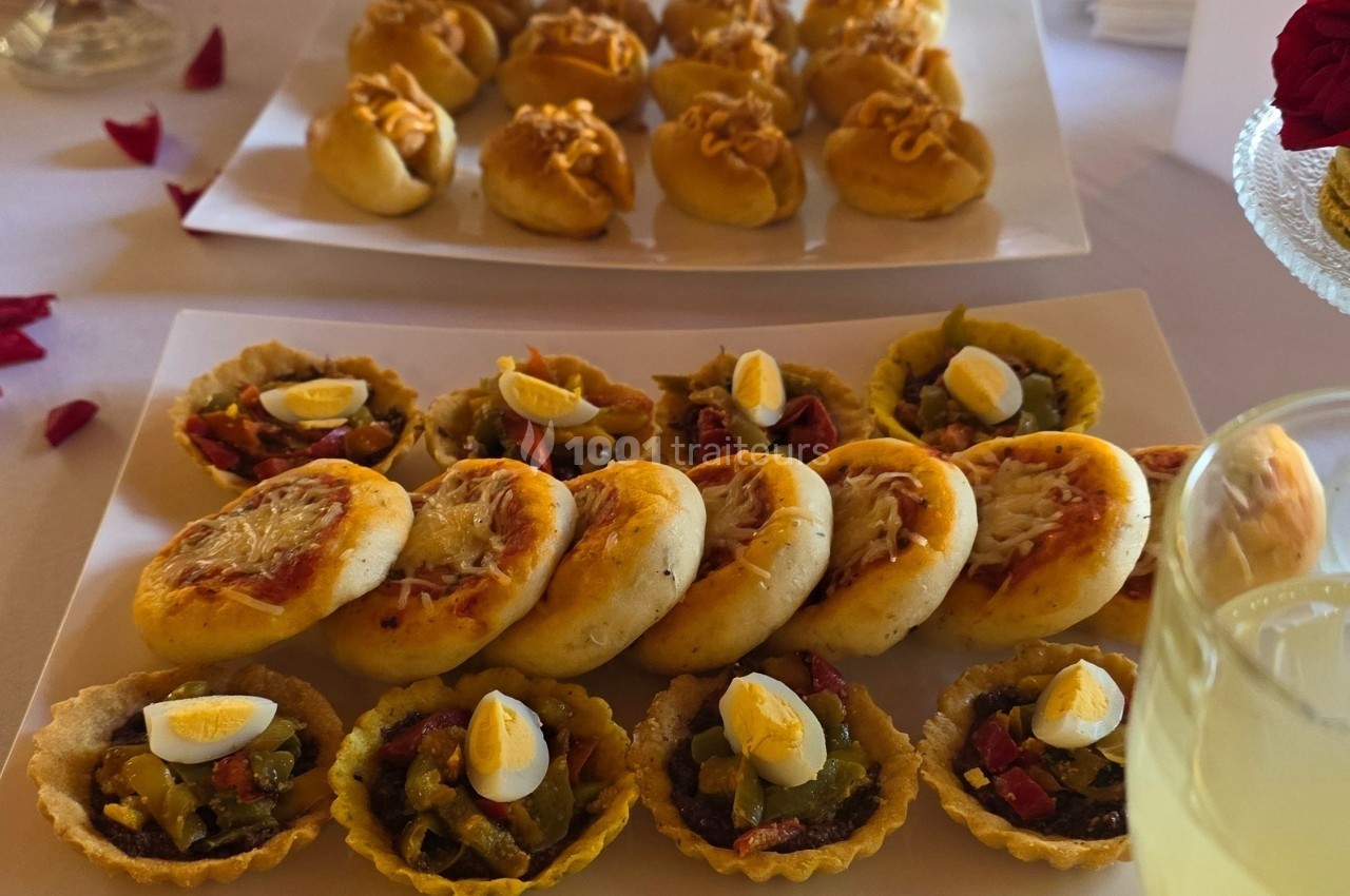 Assortiment de mini-tartelettes garnies de légumes et œufs, accompagné de petits pains garnis, présenté sur un plateau.