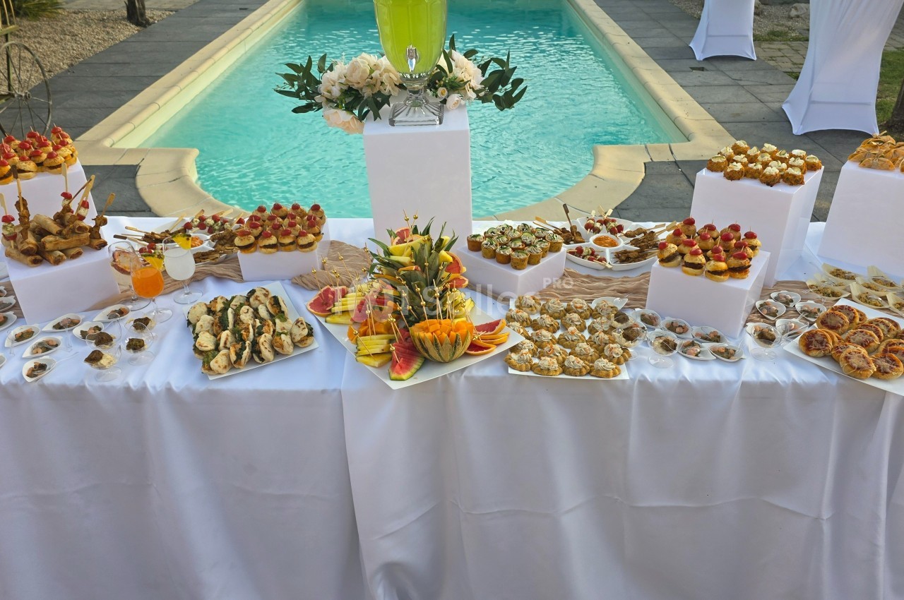 Buffet de desserts et amuse-bouches variés disposés sur une table blanche près d'une piscine.