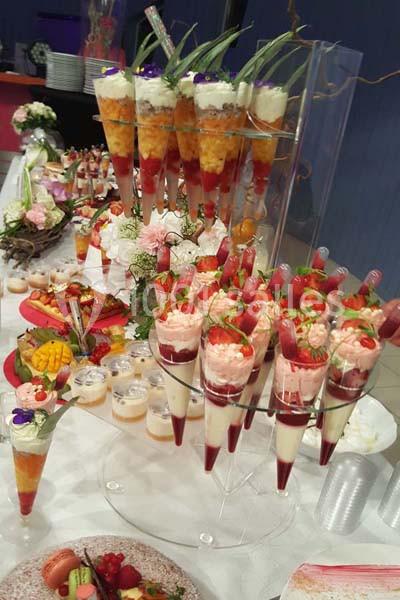 Présentoir de verrines colorées et desserts variés disposés sur une table de buffet décorée avec des fleurs.