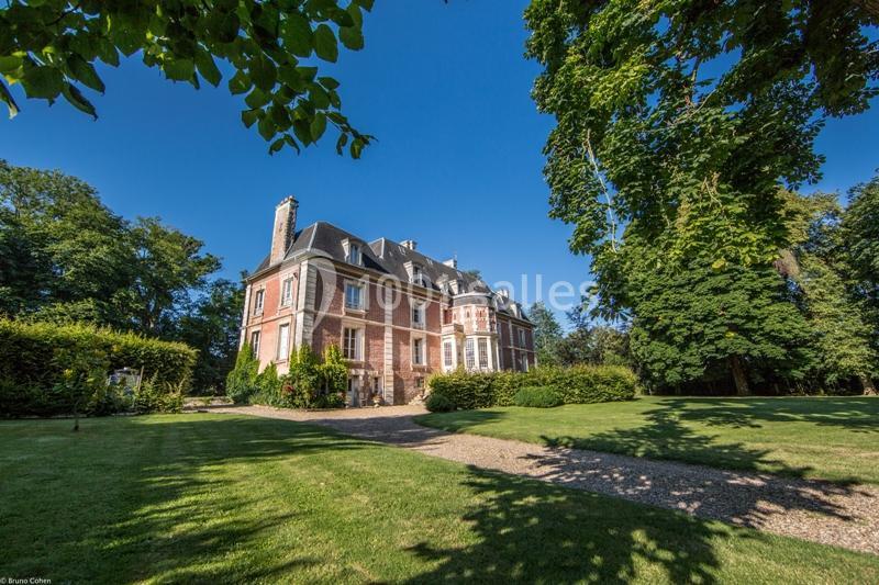Manoir en briques entouré d'un jardin verdoyant, sous un ciel bleu dégagé.