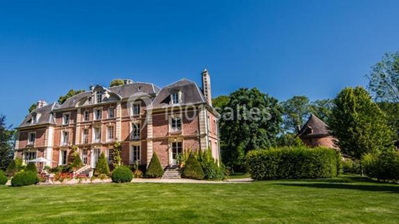 Manoir en briques entouré d'un grand jardin verdoyant sous un ciel bleu dégagé.