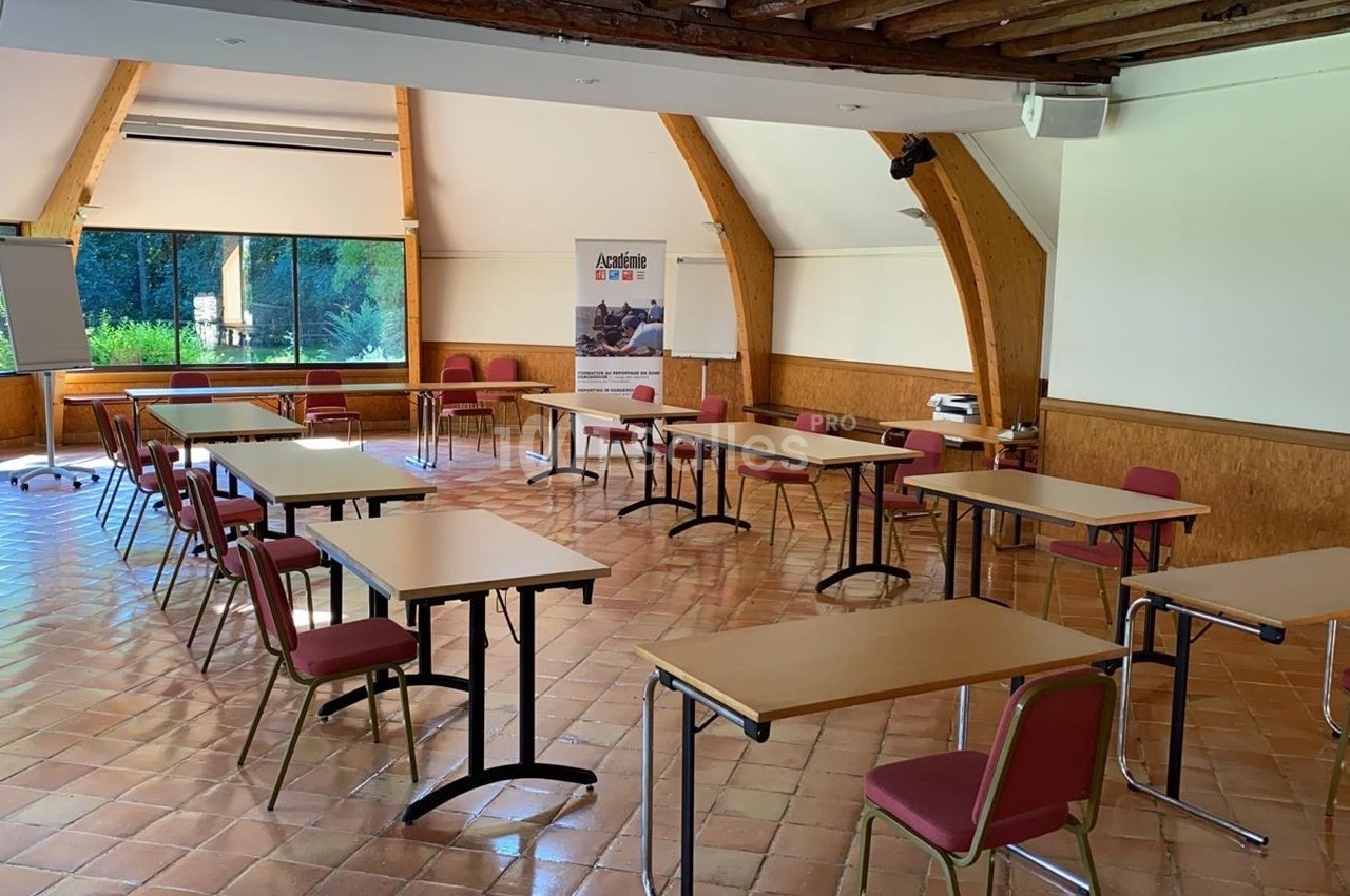 Salle de réunion lumineuse avec des tables et chaises disposées en U, un tableau blanc et un vidéoprojecteur.