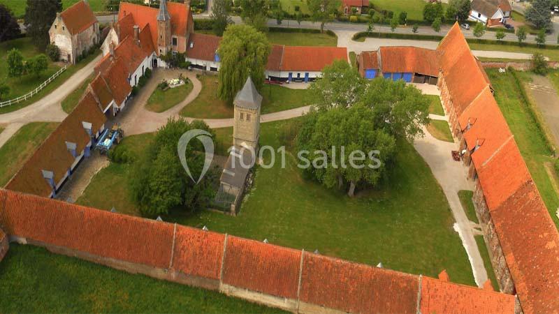 Vue aérienne d'une ferme en U avec des toits en tuiles rouges, une chapelle centrale et des arbres dans la cour.
