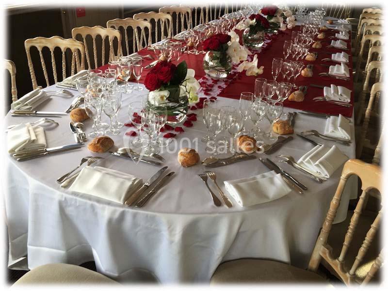 Table dressée pour un repas festif avec nappes blanches, décorations rouges, verres, couverts et petits pains.