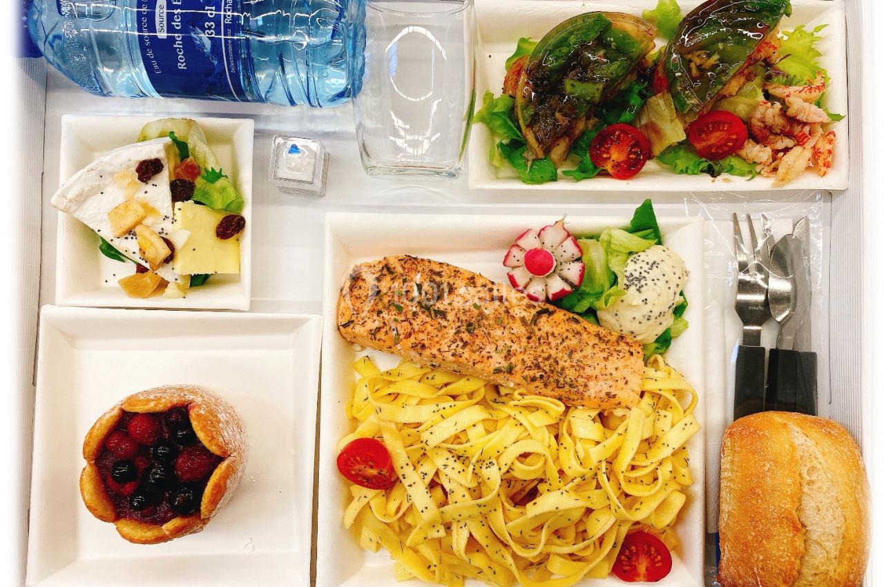Plateau-repas composé de tagliatelles au saumon, salade, fromage, dessert aux fruits rouges, pain et bouteille d'eau.