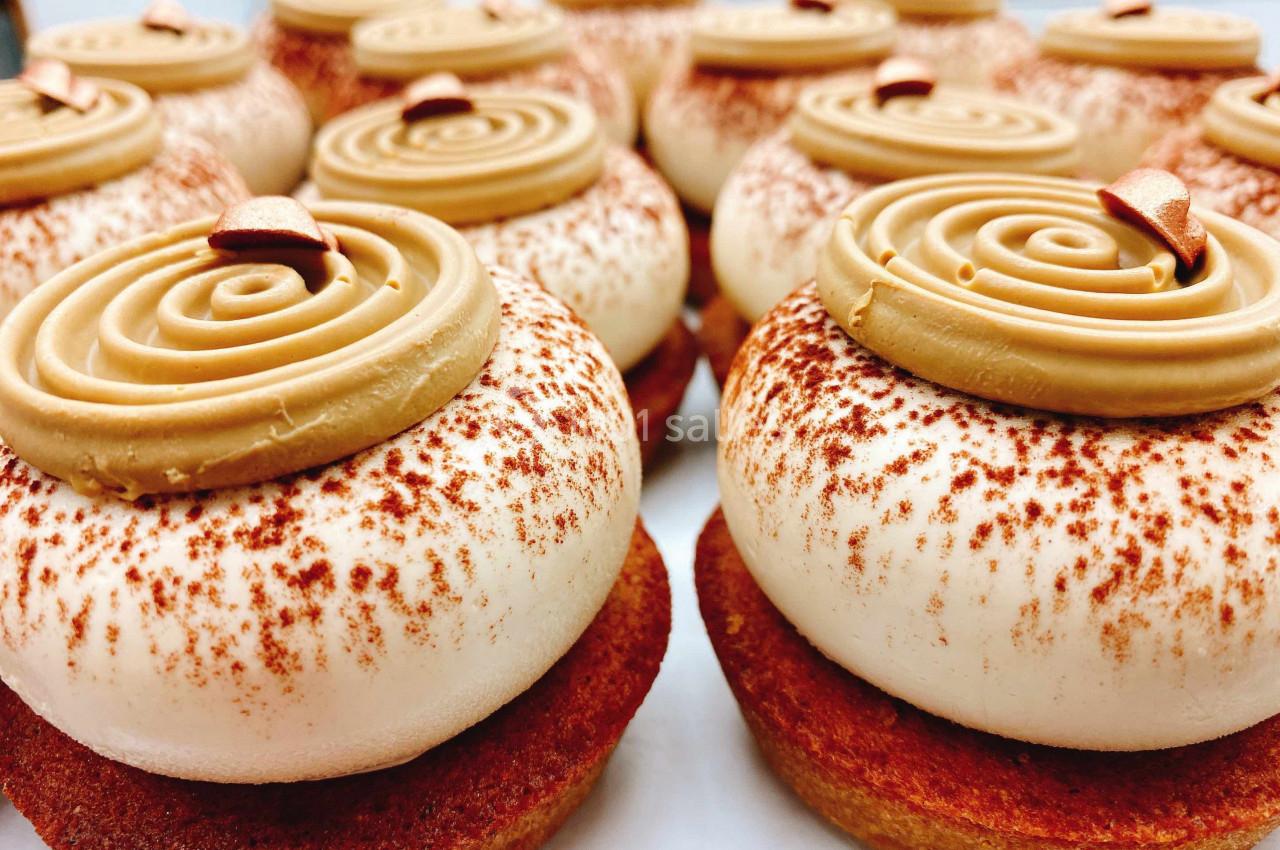 Pâtisseries individuelles garnies de crème beige tourbillonnée et saupoudrées de cacao sur une base dorée.