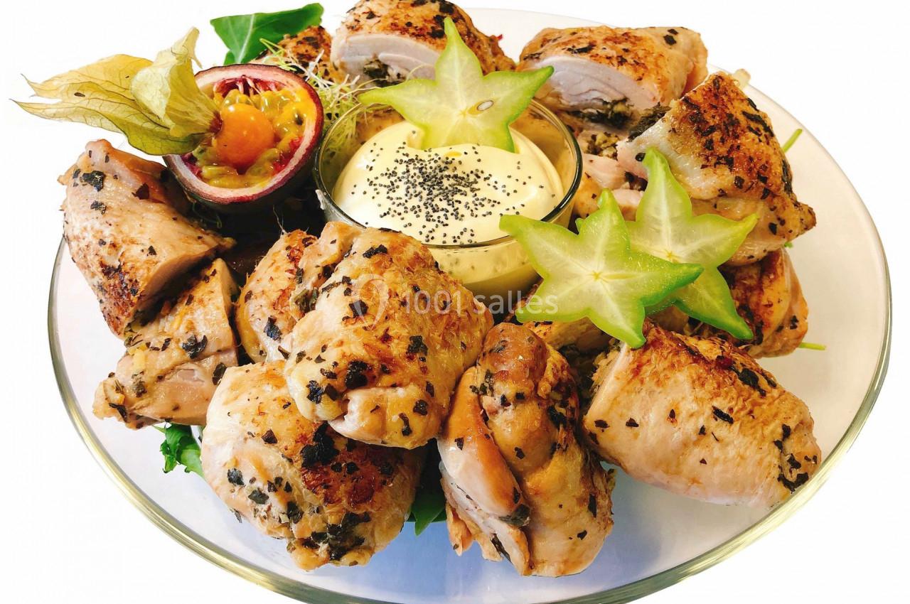 Assiette de roulés de poulet grillés garnis d'herbes, accompagnés de sauce, fruits exotiques et décoration de carambole.