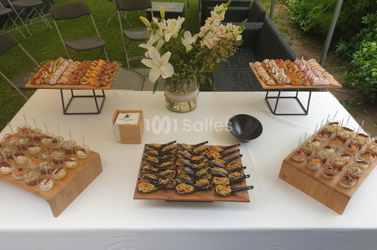Buffet en extérieur avec verrines, bouchées salées et sucrées, disposées sur une table blanche décorée de fleurs.