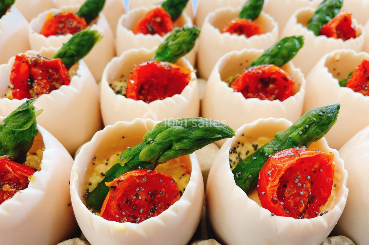 Œufs évidés garnis de tomates cerises rôties, asperges et assaisonnement, présentés en rangées.