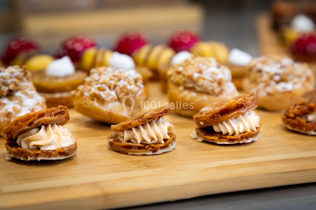 Assortiment de pâtisseries sur une planche en bois, comprenant choux, tartelettes et biscuits garnis de crème.