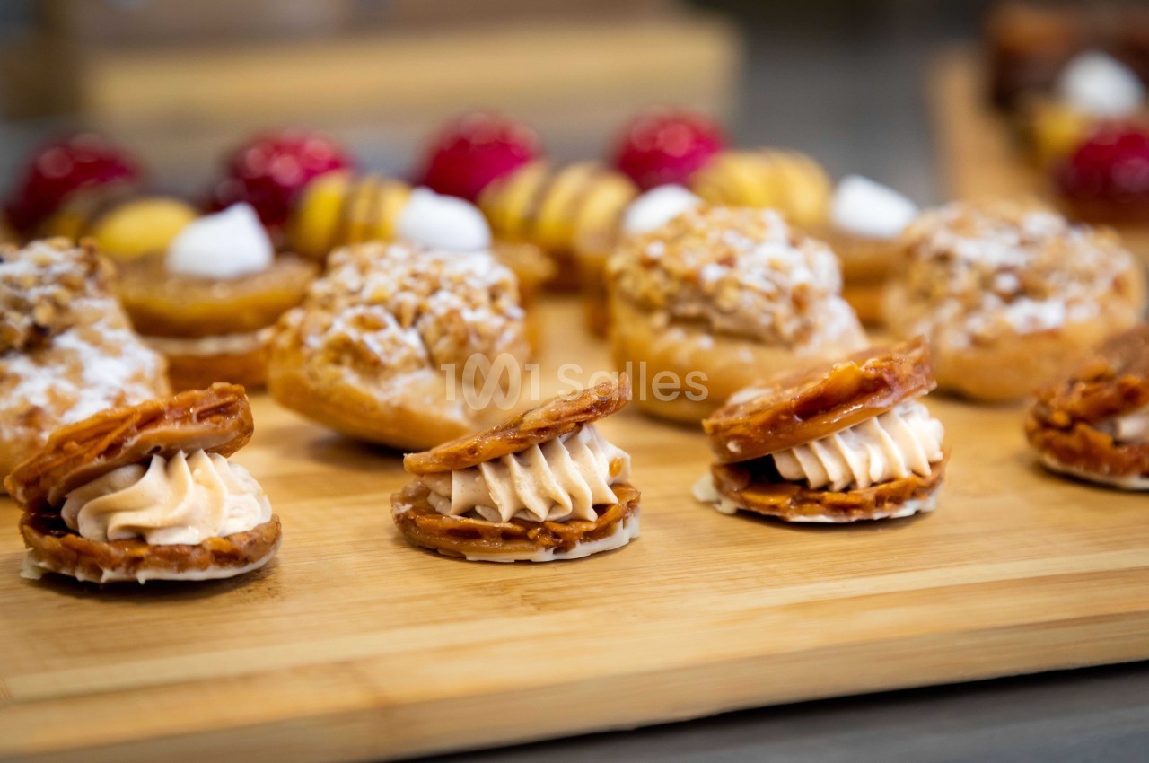 Assortiment de pâtisseries sur une planche en bois, comprenant choux, tartelettes et biscuits garnis de crème.
