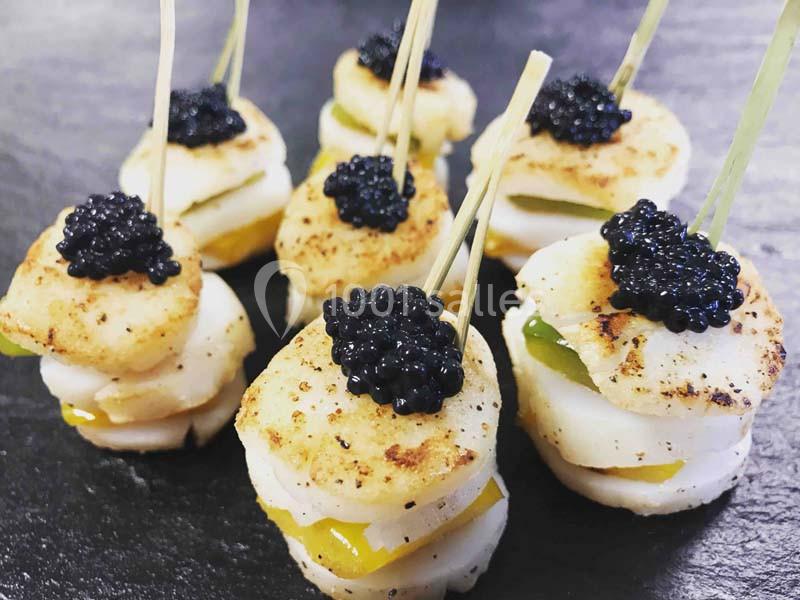Bouchées de noix de Saint-Jacques grillées garnies de caviar noir et piquées sur des brochettes, présentées sur une ardoise.