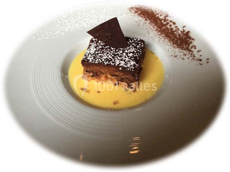 Gâteau au chocolat sur lit de crème anglaise, décoré de sucre glace, d'une tuile en chocolat et de cacao en poudre.