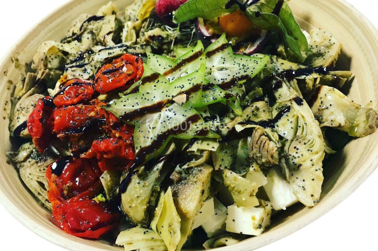 Salade composée avec artichauts, tomates confites, fromage, graines de pavot et filet de sauce balsamique.