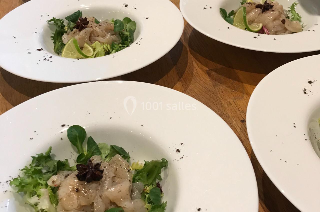 Assiettes de carpaccio de poisson avec salade verte, rondelles de citron vert et étoile de badiane sur une table en bois.