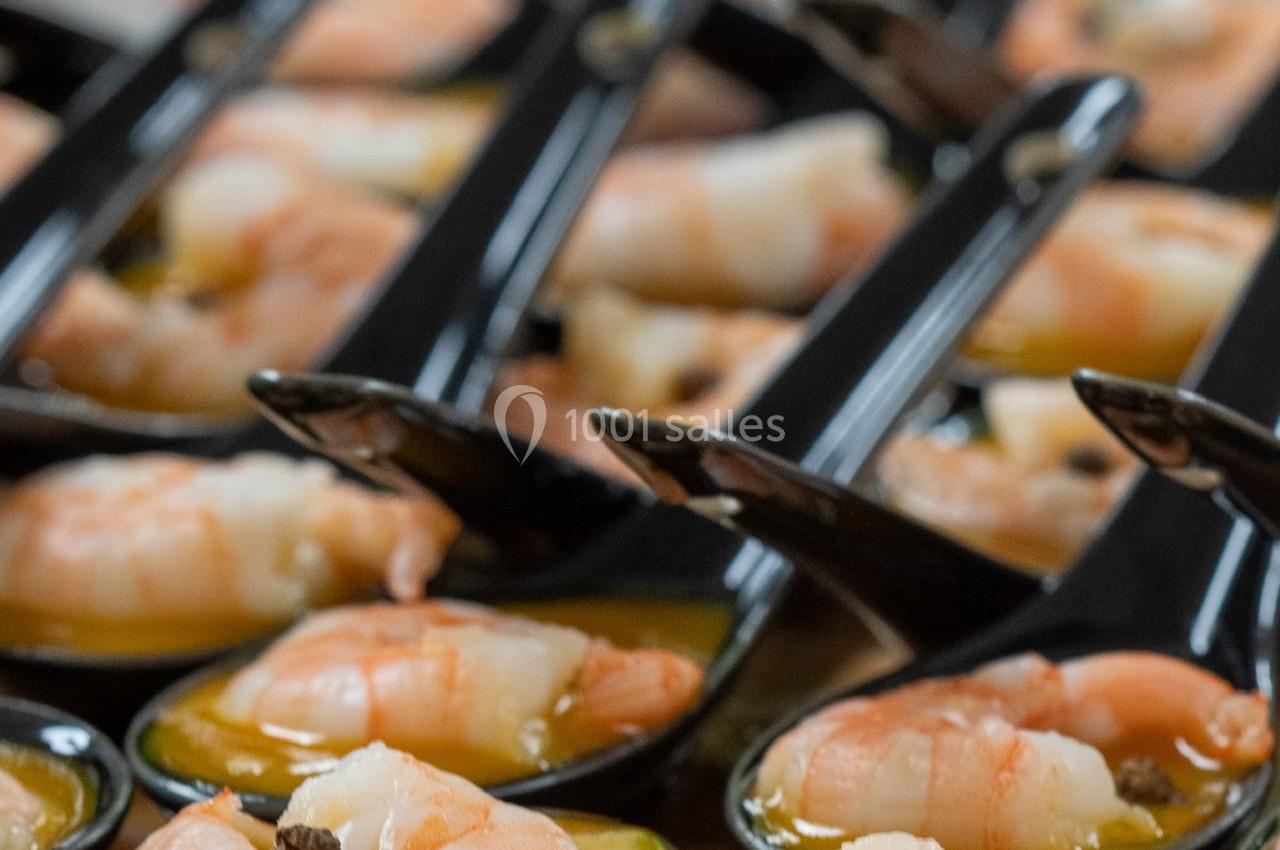Crevettes servies dans des cuillères noires avec une sauce, présentées sur une table en bois.