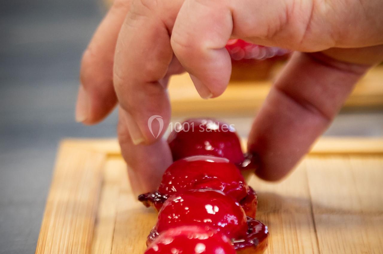 Main disposant des petites tartelettes garnies d'un glaçage rouge brillant sur une planche en bois.