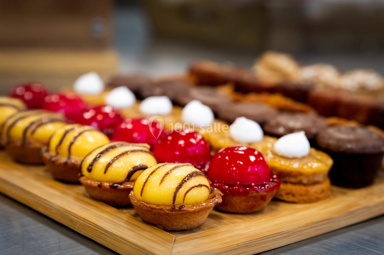 Plateau en bois garni de petites pâtisseries colorées, dont des tartelettes jaunes et rouges décorées de glaçage.